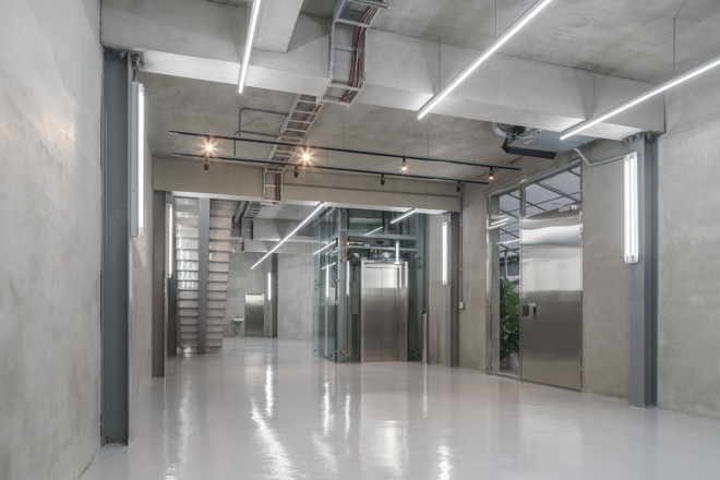 first floor of a revitalised lift factory with grey conrete walls, a shining and reflecting floor and lamps and walls and ceiling 