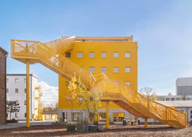 Atelier Gardens neues Eingangsgebäude in Gelb mit großer Hintertreppe